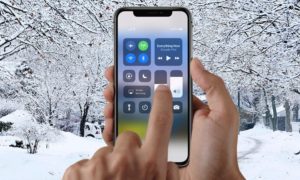 Ruka ovládající iPhone X s otevřeným ovládacím centrem na pozadí zasněžené krajiny
