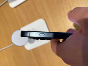 Ruka drží iPhone z boku, na titanovém rámu jsou vidět tmavé fleky