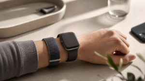 Textilní fitness náramek bez displeje na zápěstí vedle Apple Watch