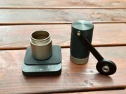 Recenze Wacaco Exagram Pro: kapesní váha pro dokonalé espresso Váha Wacaco Exagram Pro s nádobkou namleté kávy a ručním mlýnkem Wacaco Exagrind na dřevěném stole