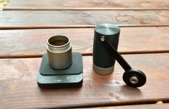Recenze Wacaco Exagram Pro: kapesní váha pro dokonalé espresso Váha Wacaco Exagram Pro s nádobkou namleté kávy a ručním mlýnkem Wacaco Exagrind na dřevěném stole